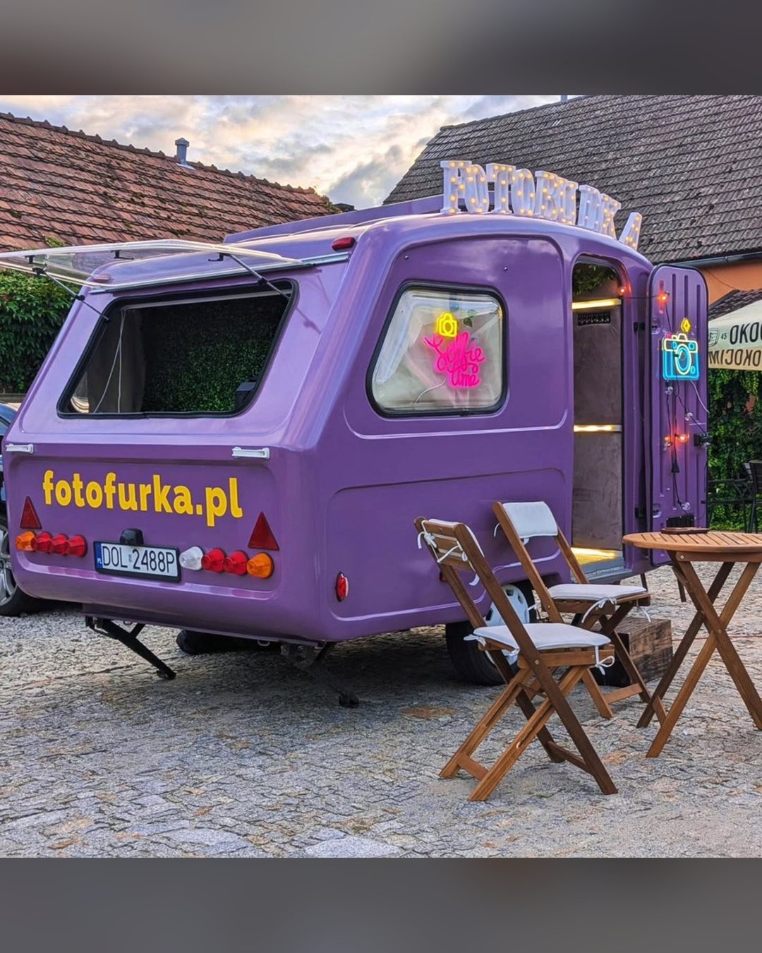Fioletowa fotoprzyczepa Fotofurka z tyłu, ze stolikiem i krzesłami na imprezie